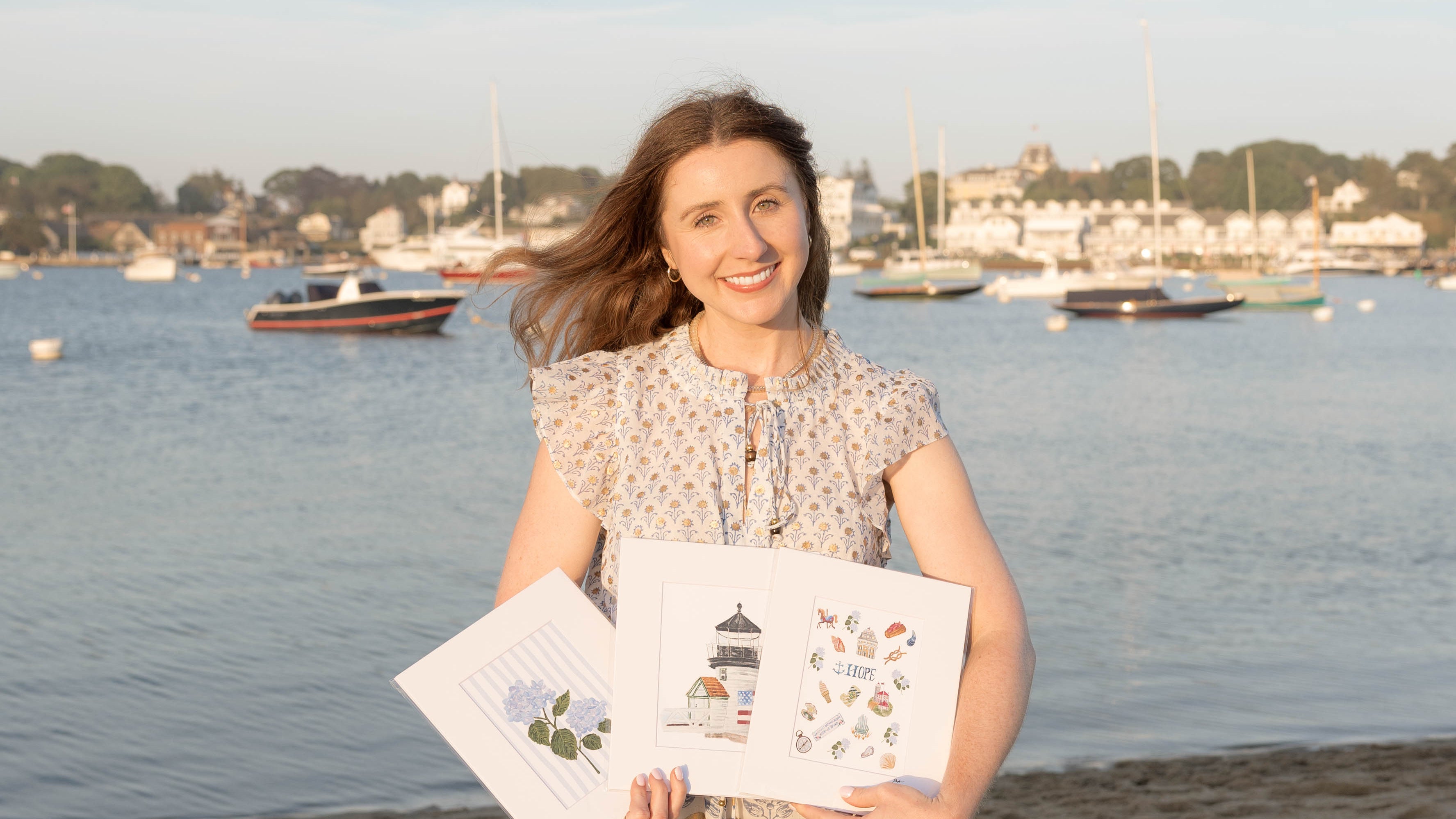 A young woman standing on a beach with three nautical prints in her hand.
